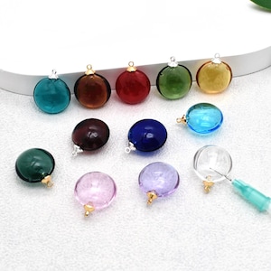 May include: A collection of colorful glass orb pendants in various shades, including teal, brown, red, green, yellow, purple, blue, and clear. Each orb has a small metal cap and loop for hanging, perfect for jewelry making or crafting.