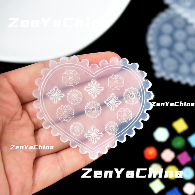 May include: A transparent, heart-shaped silicone mould with a scalloped edge and floral patterns. The mould features various flower designs and is held in a hand. The text "ZenYaChina" is visible in the image.