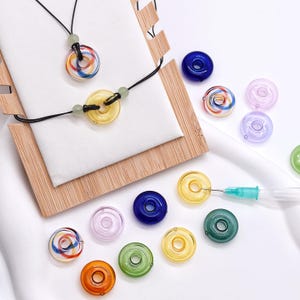 May include: A selection of colourful glass beads and jewellery. The image shows a necklace and bracelet with circular, swirled beads in red, blue, and yellow. Additional beads in various colours are scattered around.