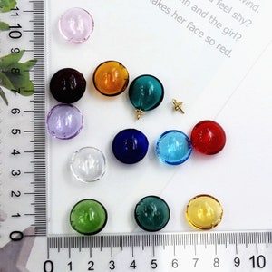 May include: Assortment of 12 round glass beads in various colors, including clear, pink, red, orange, yellow, green, blue, and purple. The beads are approximately 1 inch in diameter and have a smooth, glossy finish.