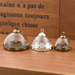 May include: Three glass dome pendant charms with ornate metal rims. The largest dome is bronze, the middle dome is silver, and the smallest dome is bronze.