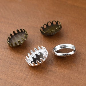 May include: Four metal bezel settings for jewelry making. Two are silver and two are bronze. The bezels have a decorative crown-like edge.