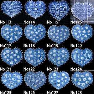 May include: A selection of blue heart-shaped nail art moulds. Each mould features a different design, including bows, flowers, and letters. The moulds are numbered from 113 to 128.