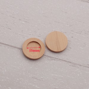 May include: Two round wooden discs, one with a 15mm diameter hole in the center. The discs are made of light brown wood and are perfect for crafting projects.