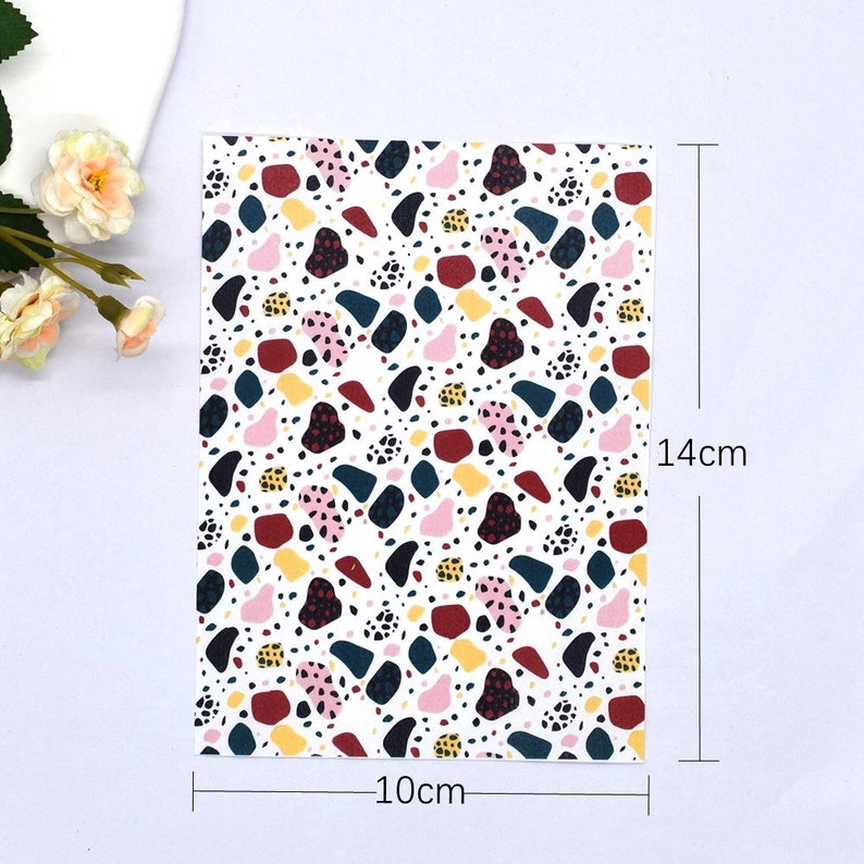 May include: A white fabric with a repeating pattern of colourful abstract shapes. The fabric measures 10 cm by 14 cm.