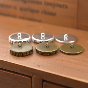 Puede incluir: Seis botones redondos de metal con un borde decorativo. Tres botones son plateados y tres son de bronce.