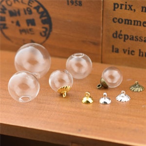 May include: A collection of clear glass globe pendants with gold and silver metal caps. The globes are various sizes and are arranged on a wooden surface.
