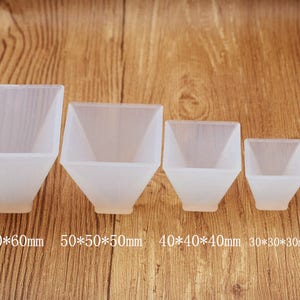 Pode incluir: Cinco moldes de pirâmide de silicone transparente de diferentes tamanhos. Os moldes estão dispostos do maior para o menor, sendo o maior de 60x60x60mm e o menor de 20x20x20mm.