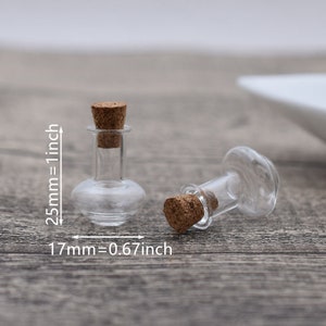 May include: Two small clear glass bottles with cork stoppers. The bottles are about 1.7 inches tall and 0.67 inches wide. The bottles are on a wooden surface.