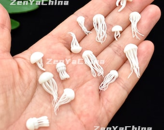 Puede incluir: Una colección de pequeñas figuras de medusas blancas con tentáculos detallados y partes superiores redondeadas. Las figuras están dispersas sobre una mano, mostrando su delicado diseño. La imagen está bien iluminada, resaltando la textura y forma de cada pieza.
