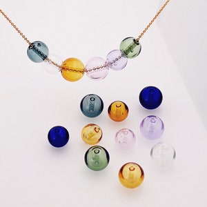 May include: A necklace with a gold chain and colorful glass beads. The beads are in shades of green, blue, purple, and yellow. There are also several loose beads in various colors, including clear, blue, green, yellow, and purple.