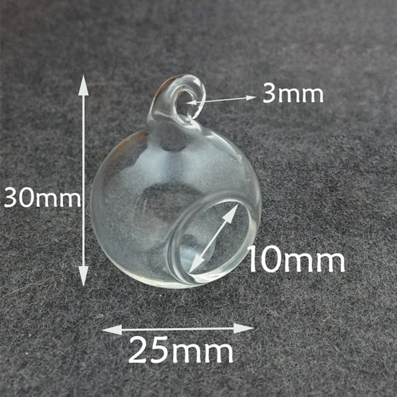 May include: A clear glass globe with a 3 mm opening at the top. The globe is 25 mm wide and 30 mm tall. The opening is 10 mm in diameter.