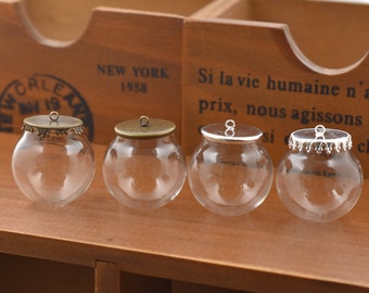 May include: Four glass globe ornaments with metal lids. The lids have a decorative design and a loop for hanging. The globes are clear and appear to be empty.
