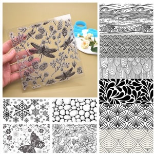 May include: A set of 10 clear transparent rubber stamps with various black and white designs. The designs include snowflakes, pebbles, flowers, dragonflies, waves, and geometric patterns.