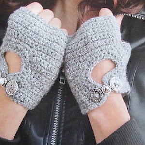 Peut inclure: Gants sans doigts gris avec une ouverture en forme de cœur et des boutons argentés. Les gants sont faits d'un fil doux et texturé.