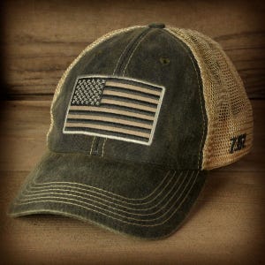 May include: A dark green and brown baseball cap with a mesh back. The front of the cap features a distressed American flag patch.