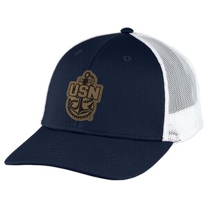 May include: A navy blue baseball cap with a white mesh back and a tan patch on the front. The patch features a dark brown anchor graphic with the letters USN centered in a bold font, surrounded by a chain design and a stitched border detail.