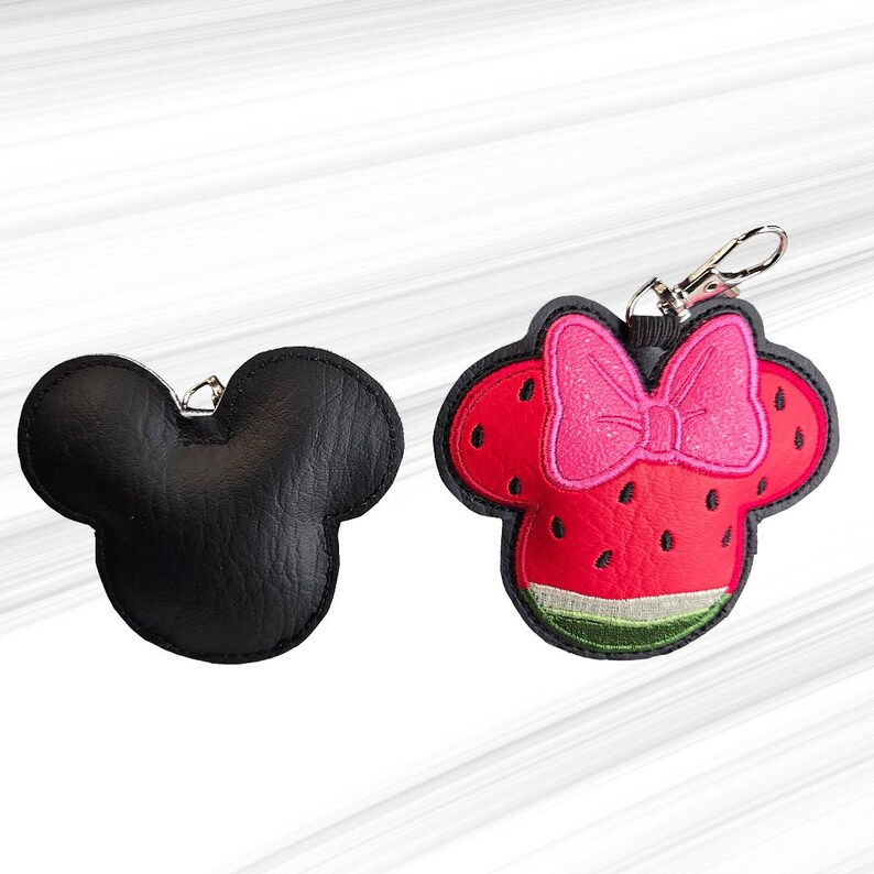 K&ouml;nnte beinhalten: Zwei Schl&uuml;sselanh&auml;nger in Form eines M&auml;usekopfes. Einer ist einfarbig schwarz, der andere ist rot mit einer rosa Schleife und Wassermelonen-Design. Beide haben silberfarbene Verschl&uuml;sse zum Befestigen an Schl&uuml;sseln oder Taschen.