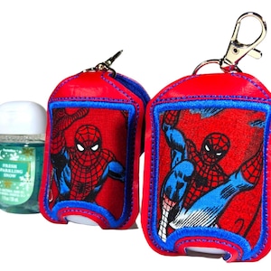 May include: Two red and blue fabric hand sanitizer holders featuring a Spider-Man graphic, each with a silver metal lobster clasp. Beside them sits a small clear plastic bottle of Fresh Sparkling Snow hand sanitizer with a white cap.