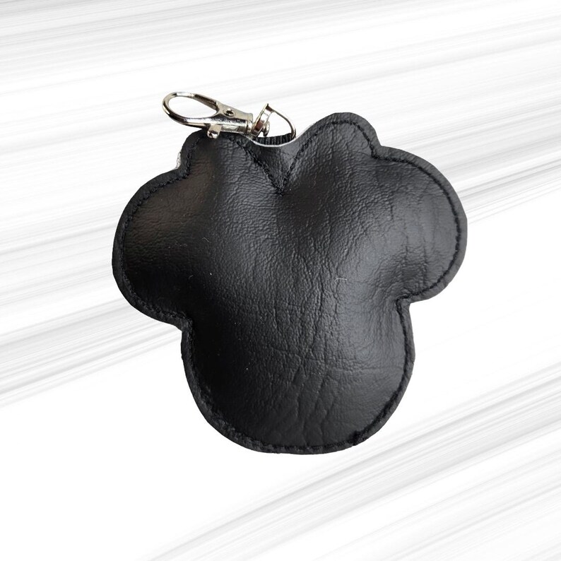 K&ouml;nnte beinhalten: Schwarzer Leder-Schl&uuml;sselanh&auml;nger in Form eines Mickey Mouse-Kopfes. Der Schl&uuml;sselanh&auml;nger hat einen silberfarbenen Verschluss zum Befestigen an Schl&uuml;sseln oder einer Tasche. Das Leder hat eine strukturierte Optik und ist an den R&auml;ndern vern&auml;ht.