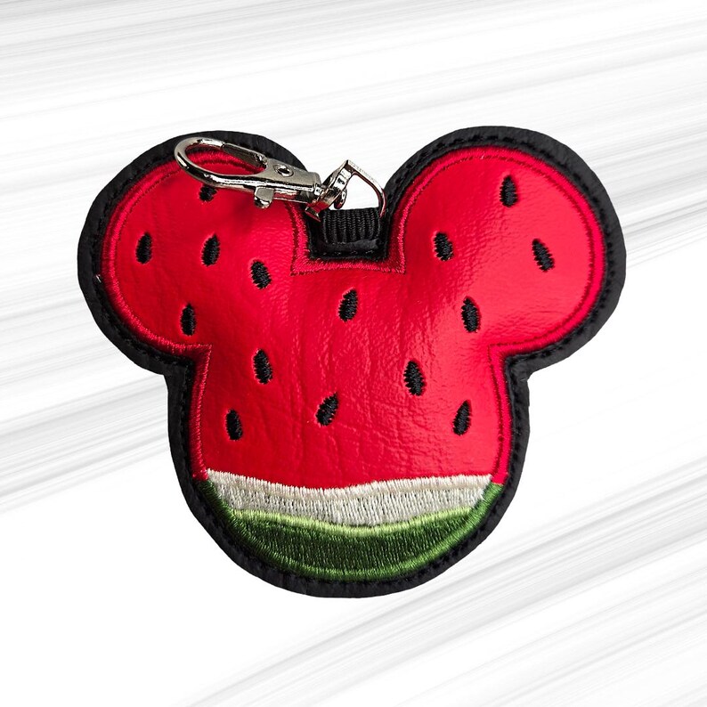 K&ouml;nnte beinhalten: Roter und schwarzer Schl&uuml;sselanh&auml;nger im Wassermelonen-Design in Form eines M&auml;usekopfes. Der Schl&uuml;sselanh&auml;nger hat einen roten K&ouml;rper mit schwarzen Samendetails, eine gr&uuml;ne und wei&szlig;e Schale und einen silbernen Verschluss.