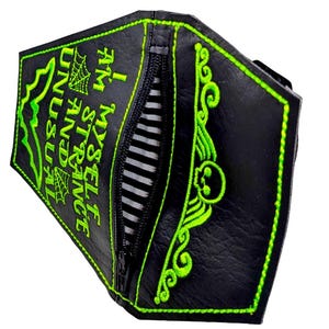 May include: A black coffin-shaped wallet with bright green embroidery featuring a skull, bat, spiderwebs, and the text I AM MYSELF STRANGE AND UNUSUAL. The wallet has a central black zip closure and an interior lining with black and white stripes.