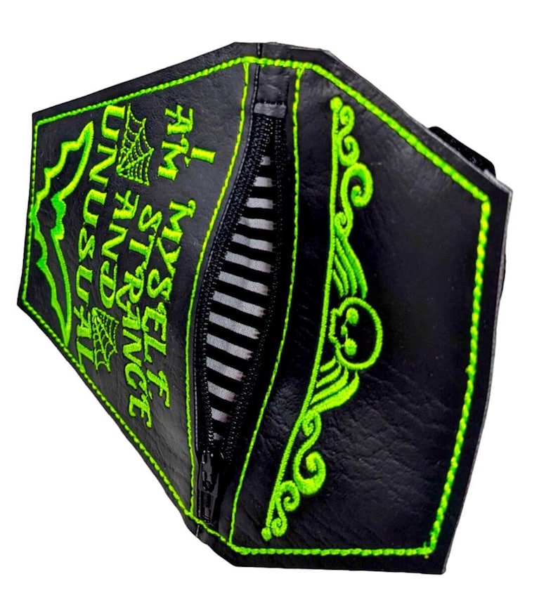 May include: A black coffin-shaped wallet with bright green embroidery featuring a skull, bat, spiderwebs, and the text I AM MYSELF STRANGE AND UNUSUAL. The wallet has a central black zip closure and an interior lining with black and white stripes.