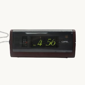 Puede incluir: Un reloj de solapa rectangular Copal con una carcasa de acabado de grano de madera marrón oscuro y un panel frontal negro. La pantalla digital muestra la hora 4:56 PM en números verdes, con un pequeño dial de alarma vertical a la izquierda.