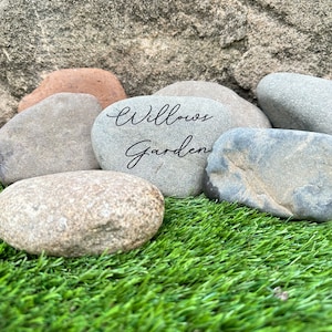 Pu&ograve; includere: Primo piano di una pietra grigia con le parole "Willows Garden" scritte su di essa. La pietra &egrave; circondata da altre pietre grigie e erba verde.