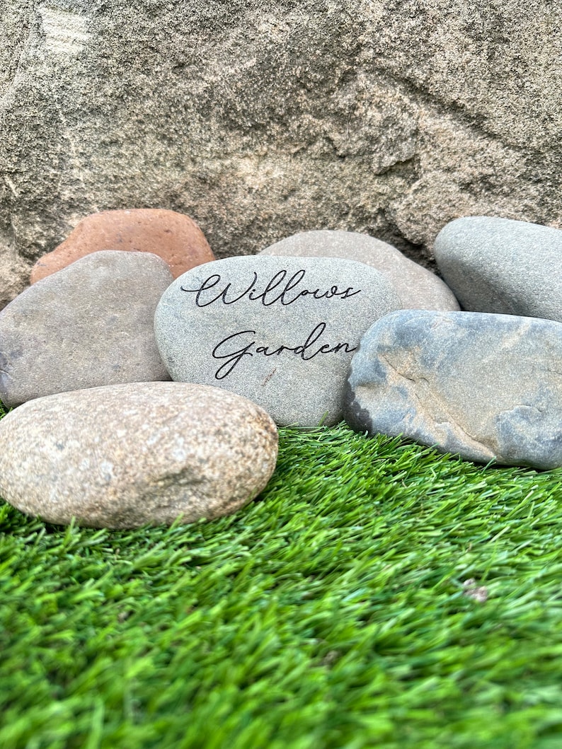 Pu&ograve; includere: Primo piano di una pietra grigia con le parole "Willows Garden" scritte su di essa. La pietra &egrave; circondata da altre pietre grigie e erba verde.