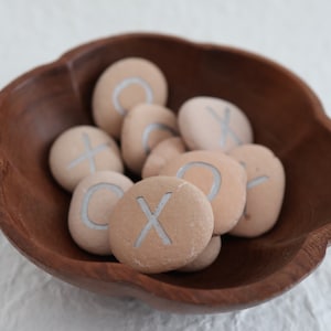 May include: A wooden bowl filled with smooth, light brown stones. Each stone has a silver 'X' or 'O' painted on it.
