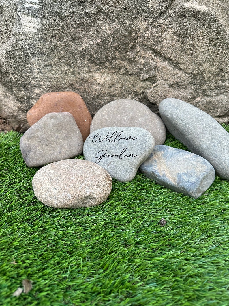 Pu&ograve; includere: Una collezione di pietre grigie, marroni e bianche su una superficie di erba artificiale verde. Una pietra ha le parole "Willow Garden" scritte su di essa.