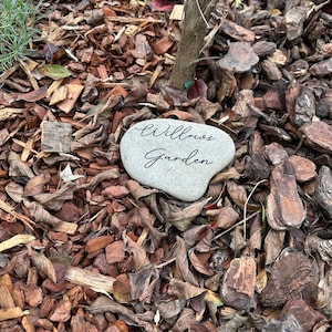 Pu&ograve; includere: Primo piano di una pietra grigia con le parole "Willows Garden" incise su di essa. La pietra &egrave; circondata da trucioli di legno marroni.