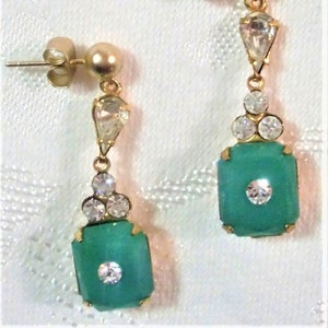 May include: Gold-toned earrings with a post back. Each earring features a teardrop-shaped clear stone, three small clear stones, and a square, turquoise-colored stone with a central clear stone. The earrings have a vintage aesthetic.
