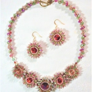 May include: A pink and green beaded necklace with a gold clasp and matching earrings. The necklace features a row of pink and green beads with a cluster of pink and green beads in the center. The earrings are small and feature a single pink bead.
