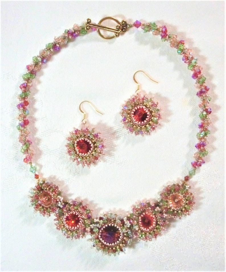 May include: A pink and green beaded necklace with a gold clasp and matching earrings. The necklace features a row of pink and green beads with a cluster of pink and green beads in the center. The earrings are small and feature a single pink bead.