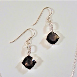 May include: A pair of silver earrings with a dark brown square gemstone and a row of small clear stones on the dangle.