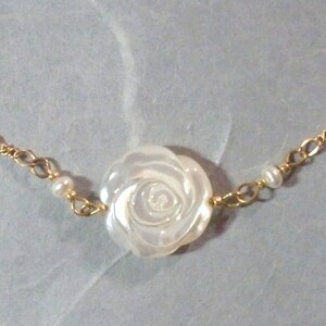 May include: A delicate gold chain necklace with a white mother-of-pearl rose pendant and small white pearl accents.