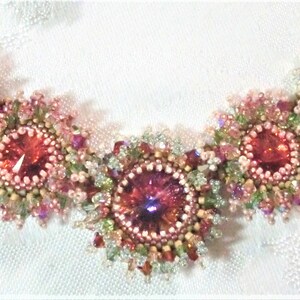 May include: A delicate necklace with five pink and green flower-shaped clusters of beads, each with a sparkling red crystal in the center.