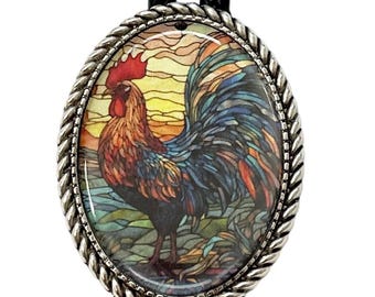 May include: Oval bolo tie with a detailed rooster design. The rooster is depicted in vibrant colors against a sunset backdrop. The silver-toned frame has a braided edge, and the tie features a black braided cord.