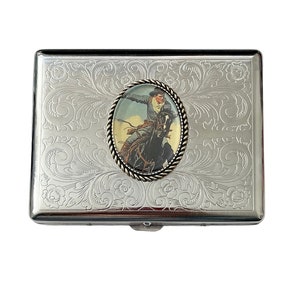 May include: Silver cigarette case with an engraved floral design and a round, silver-toned medallion featuring a cowboy riding a horse.