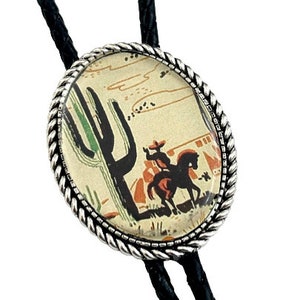 May include: A bolo tie with a silver oval pendant featuring a vintage illustration of a cowboy riding a horse in a desert landscape with a cactus. The pendant has a rope-like border. The bolo tie has black cords.
