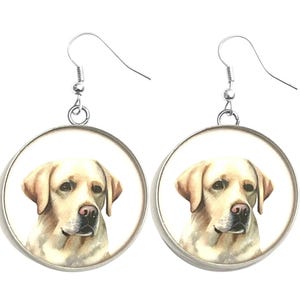 May include: A pair of round earrings featuring a detailed illustration of a yellow Labrador Retriever dog. The dog's head is centered in a silver-colored frame, with a white background. The earrings have silver-colored fish hook ear wires.