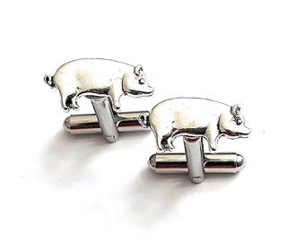 May include: A pair of silver-toned cufflinks featuring a detailed pig design. The pig is in a standing position, with its body and legs clearly defined. The cufflinks have a classic post and toggle closure.