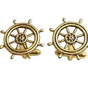 Può includere: Un paio di gemelli dorati con un design a forma di ruota di nave.