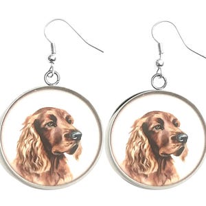 May include: A pair of round, silver-toned earrings. Each earring features a detailed portrait of a reddish-brown Irish Setter dog against a white background. The dog's fur is depicted with realistic detail, and the earrings have a simple hook closure.