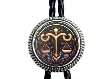 May include: A silver-toned bolo tie with a black braided cord. The circular pendant features a Libra zodiac symbol in gold and black, surrounded by a textured silver border. The design includes scales and celestial elements.