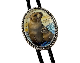 May include: A silver bolo tie with a round glass charm featuring a painted image of two sea otters, one adult and one pup, in a blue and yellow water scene.