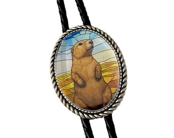 May include: A silver bolo tie with a round glass charm featuring a cartoon prairie dog standing on a colorful background.