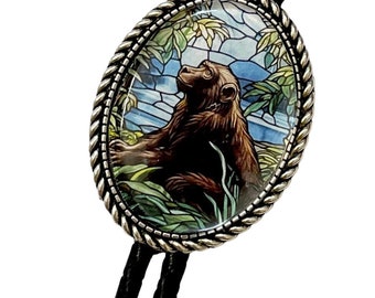May include: Oval bolo tie with a silver-toned frame and a detailed image of a brown monkey in a jungle setting. The monkey is looking up. The tie has a black braided cord.